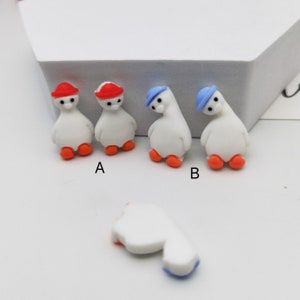 Puede incluir: Cuatro pequeñas figuritas blancas de pingüinos con sombreros rojos y azules. Los pingüinos están de pie sobre una superficie blanca. Los pingüinos tienen pies naranjas.