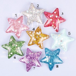 Puede incluir: Ocho adornos con forma de estrella de purpurina en varios colores, incluyendo rosa, plata, rojo, dorado, azul claro, verde, morado y azul. Cada estrella tiene un revestimiento de resina transparente y está decorada con estrellas de purpurina más pequeñas.