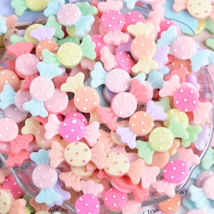 May include: A large assortment of colourful candy-shaped resin embellishments with white polka dots. The candy is in various pastel colours, including pink, blue, yellow, green, and orange.