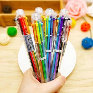 May include: A collection of six-color ballpoint pens. Each pen has a clear barrel with six different colored ink refills. The pens are held together, with the text "6color Ball Point pen" visible on one of the pens.