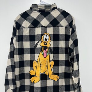 May include: Black and white plaid flannel shirt with a cartoon image of Pluto the dog on the back.