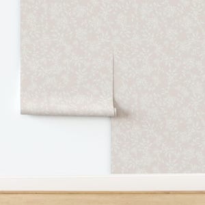 Puede incluir: Un rollo de papel tapiz de color rosa p&aacute;lido con un delicado patr&oacute;n floral blanco. El papel tapiz est&aacute; parcialmente desenrollado, revelando el patr&oacute;n.