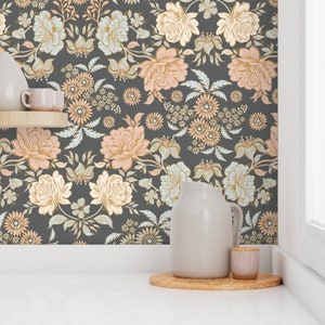 May include: Wallpaper featuring a dark gray background with a repeating floral pattern in shades of peach, cream, and pale blue. The design includes large blossoms, smaller daisy-like flowers, and leafy stems arranged in a symmetrical botanical layout.