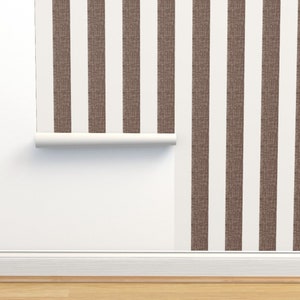 May include: A roll of brown and white striped wallpaper with a textured surface. The wallpaper is partially unrolled and hanging on a white wall.