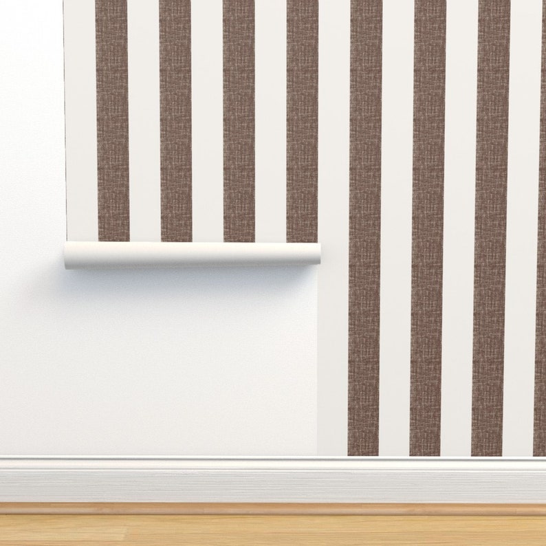 May include: A roll of brown and white striped wallpaper with a textured surface. The wallpaper is partially unrolled and hanging on a white wall.