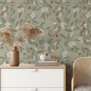 May include: A green wallpaper with a floral pattern featuring white flowers and brown leaves. A vase with dried pampas grass sits on a white dresser with two drawers. A wicker chair is in the background.