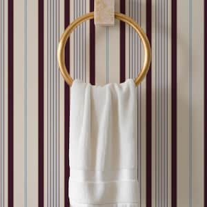 May include: A gold-colored towel ring with a white towel hanging from it. The ring is mounted on a rectangular, light-colored stone. The background is a striped wallpaper with vertical lines in cream, burgundy, and light blue.
