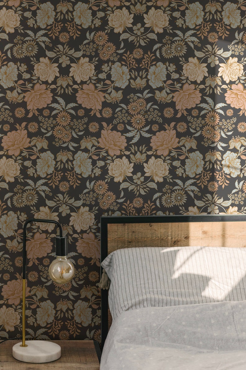 May include: Wallpaper featuring a dark charcoal background with a repeating floral pattern in muted shades of peach, light blue, and cream. The design includes various blossoms, leaves, and stems arranged in a dense, symmetrical botanical layout.
