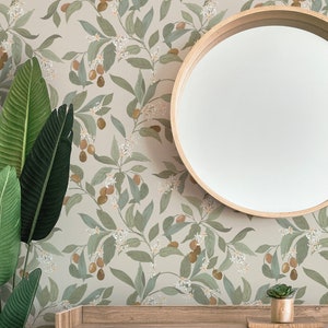 May include: A beige wallpaper with a repeating pattern of green leaves, white flowers, and brown fruit. A round wooden mirror hangs on the wall above a white dresser with a wooden top. The dresser has two drawers and the text "Paisley & Dot" is printed on the front of the bottom drawer.