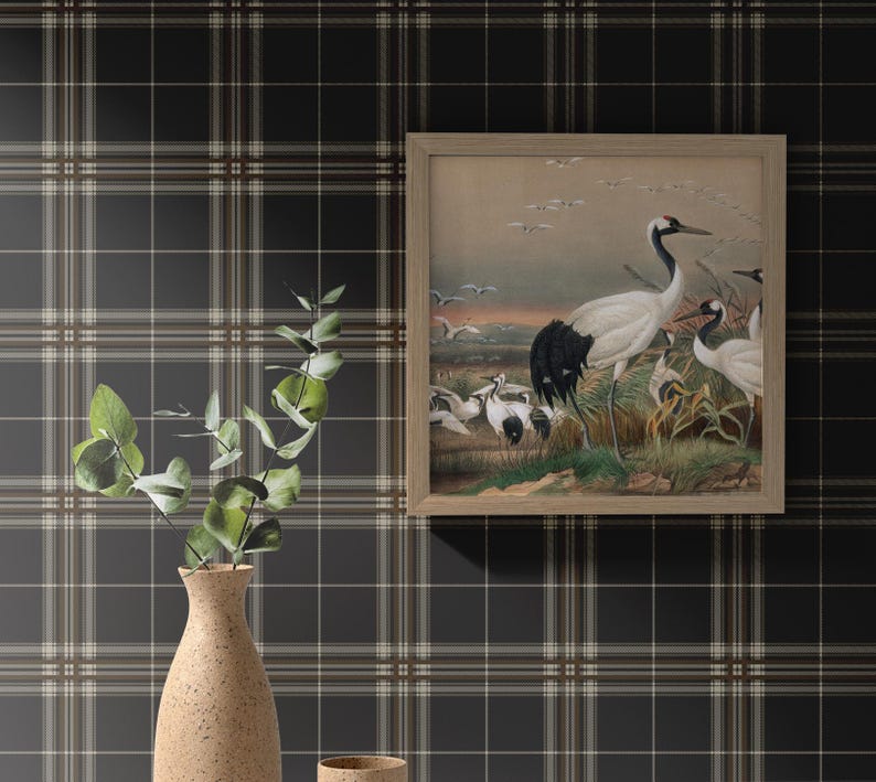 Op de afbeelding: Een ingelijste print van een zwart-witte kraanvogel met een bruine achtergrond. De print is omgeven door een lichtbruin frame en hangt aan een zwart-wit geruite muur.