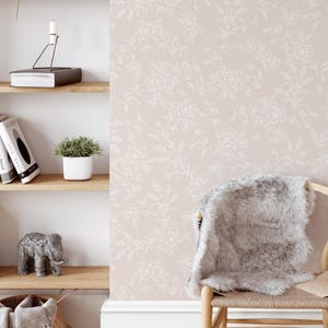 Puede incluir: Un papel tapiz rosa claro con un patr&oacute;n floral blanco. El papel tapiz se muestra en una habitaci&oacute;n con un estante de madera, una peque&ntilde;a planta en maceta y una silla con una manta blanca y esponjosa.