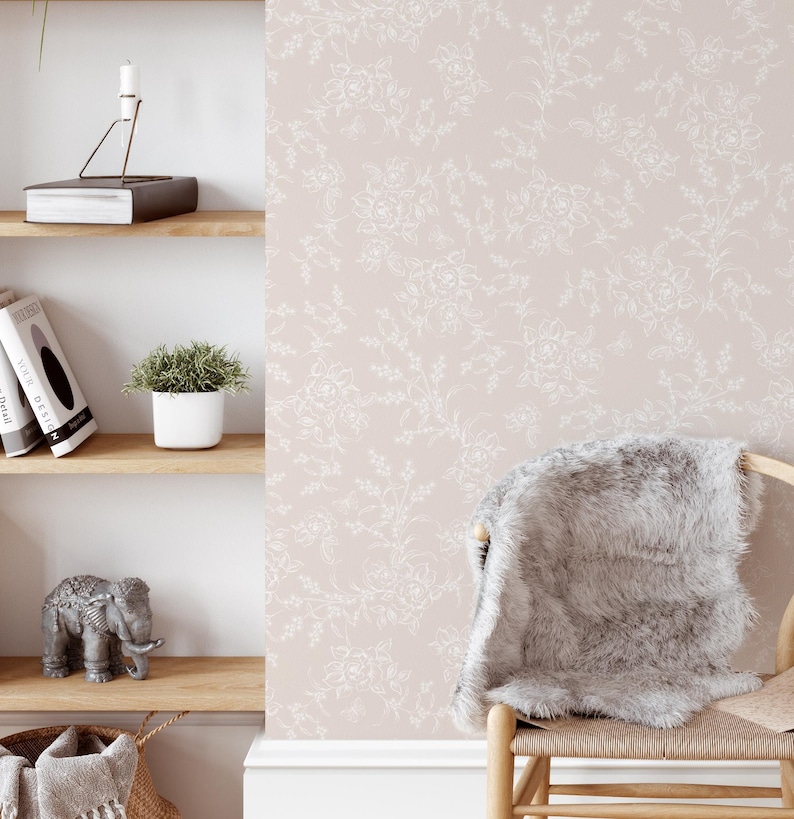 Puede incluir: Un papel tapiz rosa claro con un patr&oacute;n floral blanco. El papel tapiz se muestra en una habitaci&oacute;n con un estante de madera, una peque&ntilde;a planta en maceta y una silla con una manta blanca y esponjosa.