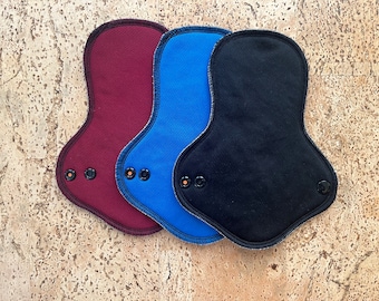 May include: Three reusable cloth menstrual pads in burgundy, blue, and black.