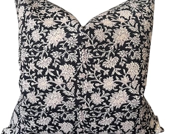 May include: A square decorative pillow with a black background and a repeating floral pattern in off-white. The pillow has a soft, textured appearance and is likely made of fabric. The floral design features detailed blossoms and leaves.