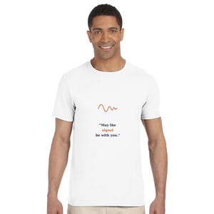 以下が含まれることがあります： 白い半袖Tシャツで、胸の中央に小さなオレンジ色の波線のグラフィックと「May the signal be with you.」というテキストがプリントされています。「signal」という単語はオレンジ色で、その他のテキストは黒色で表記されています。