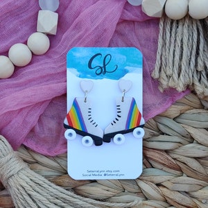 May include: Rainbow roller skate earrings with white wheels and a white heart charm. The earrings are on a white card with the text "Seterralynn.etsy.com" and "Social Media @Seterralynn".
