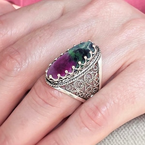 May include: A silver ring with a large oval-shaped green and pink gemstone set in a filigree design.