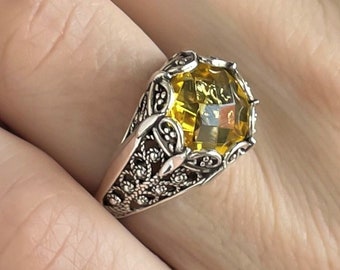 May include: A silver ring with a large, yellow gemstone set in a detailed, ornate design.
