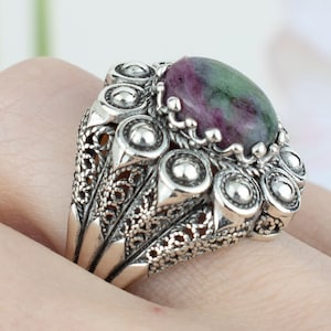 May include: A silver ring with an intricate filigree design and a green and pink gemstone in the center.