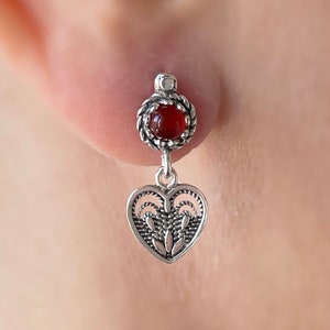 May include: Silver earrings with a red carnelian stone and a heart-shaped dangle. The heart has a delicate filigree design.
