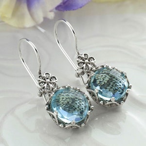 May include: A pair of silver earrings with blue gemstone drops and floral accents.