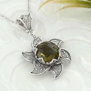 May include: A silver necklace with a green gemstone pendant. The pendant is a flower design with intricate filigree details.