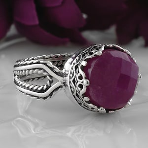 May include: A silver ring with a large, faceted, purple gemstone set in a detailed, ornate crown-like setting. The ring band is twisted and has a rope-like design.