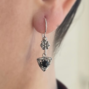May include: Silver dangle earrings with a black gemstone in a triangular setting and a floral design above.