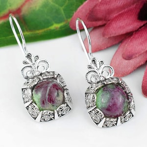 May include: A pair of silver dangle earrings with green and pink gemstone cabochons set in ornate filigree frames.