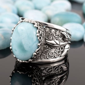 May include: A silver ring featuring a large oval blue gemstone set in a filigree design.