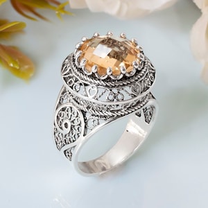 May include: A silver ring with an intricate filigree design and a large, oval-shaped, light brown gemstone.