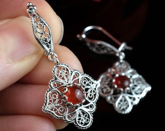 May include: A pair of silver filigree earrings featuring red carnelian gemstones. The earrings are delicate and intricate, with a floral design.