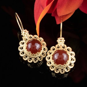 May include: A pair of gold earrings with red carnelian gemstones. The earrings have a delicate filigree design.