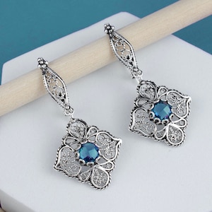 Puede incluir: Un par de pendientes de filigrana de plata con detalles de piedras preciosas azules. Los pendientes presentan un diseño delicado e intrincado y son perfectos para añadir un toque de elegancia a cualquier atuendo.