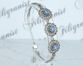 Puede incluir: Una pulsera de plata con tres eslabones circulares en forma de flor, cada uno con una piedra preciosa azul redonda en el centro rodeada de pequeñas piedras claras. La pulsera tiene un diseño de cadena delicada y un cierre seguro.