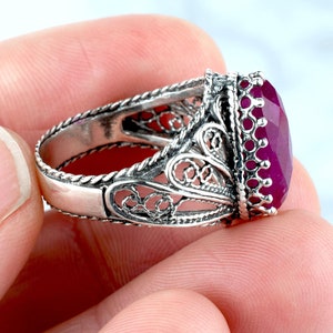 May include: A silver filigree ring with a large, oval-shaped, deep pink gemstone.