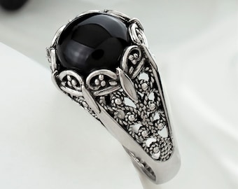 May include: A silver ring with a black gemstone set in a filigree design.