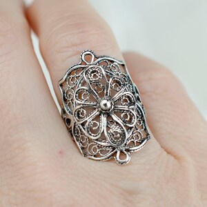 May include: A silver filigree ring with a floral design. The ring is wide and has a delicate, intricate pattern.