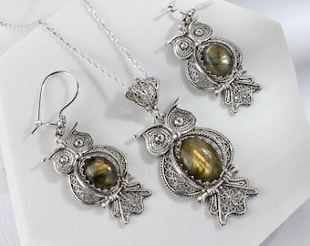 May include: A silver owl necklace and earrings set with a green gemstone. The owl is detailed with filigree work.