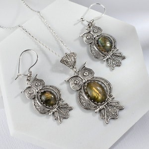 May include: A silver owl necklace and earrings set with a green gemstone. The owl is detailed with filigree work.