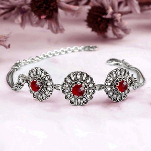 May include: Silver bracelet with three red gemstone accents in a floral design.