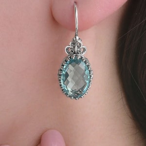 Puede incluir: Pendientes de plata con una piedra ovalada azul claro engastada en un diseño de filigrana.