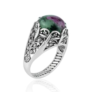 May include: A silver ring with an intricate filigree design and a green and pink gemstone.
