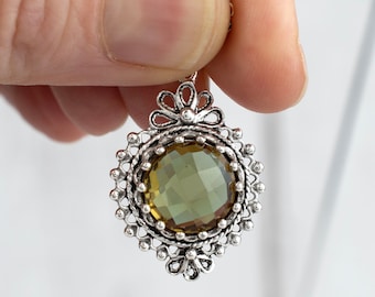 May include: A silver pendant necklace with a large, faceted, olive green gemstone set in a detailed, ornate silver frame.