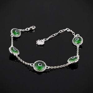 Puede incluir: Un brazalete de cadena de plata con cinco dijes de ojo turco verde. Cada dije tiene un centro blanco y está rodeado por un borde plateado.