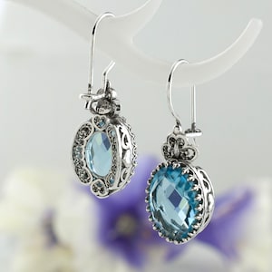 May include: A pair of silver earrings with blue gemstone accents. The earrings feature a delicate filigree design and a round, faceted gemstone.