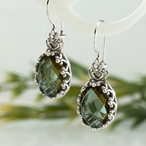 May include: A pair of silver dangle earrings with a green gemstone in a detailed filigree setting.