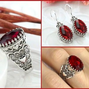 May include: A silver ring and earrings set with a large red gemstone. The ring has a filigree design with hearts and the earrings are dangle style.