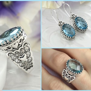 May include: A set of silver earrings and a ring with a blue gemstone. The earrings are dangle earrings with a heart-shaped design. The ring has a large oval-shaped gemstone surrounded by a filigree design.