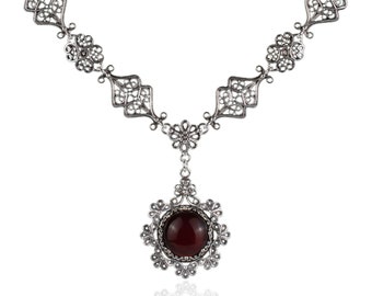 May include: A silver filigree necklace with a red gemstone pendant. The pendant is a round cabochon stone set in a silver filigree design.